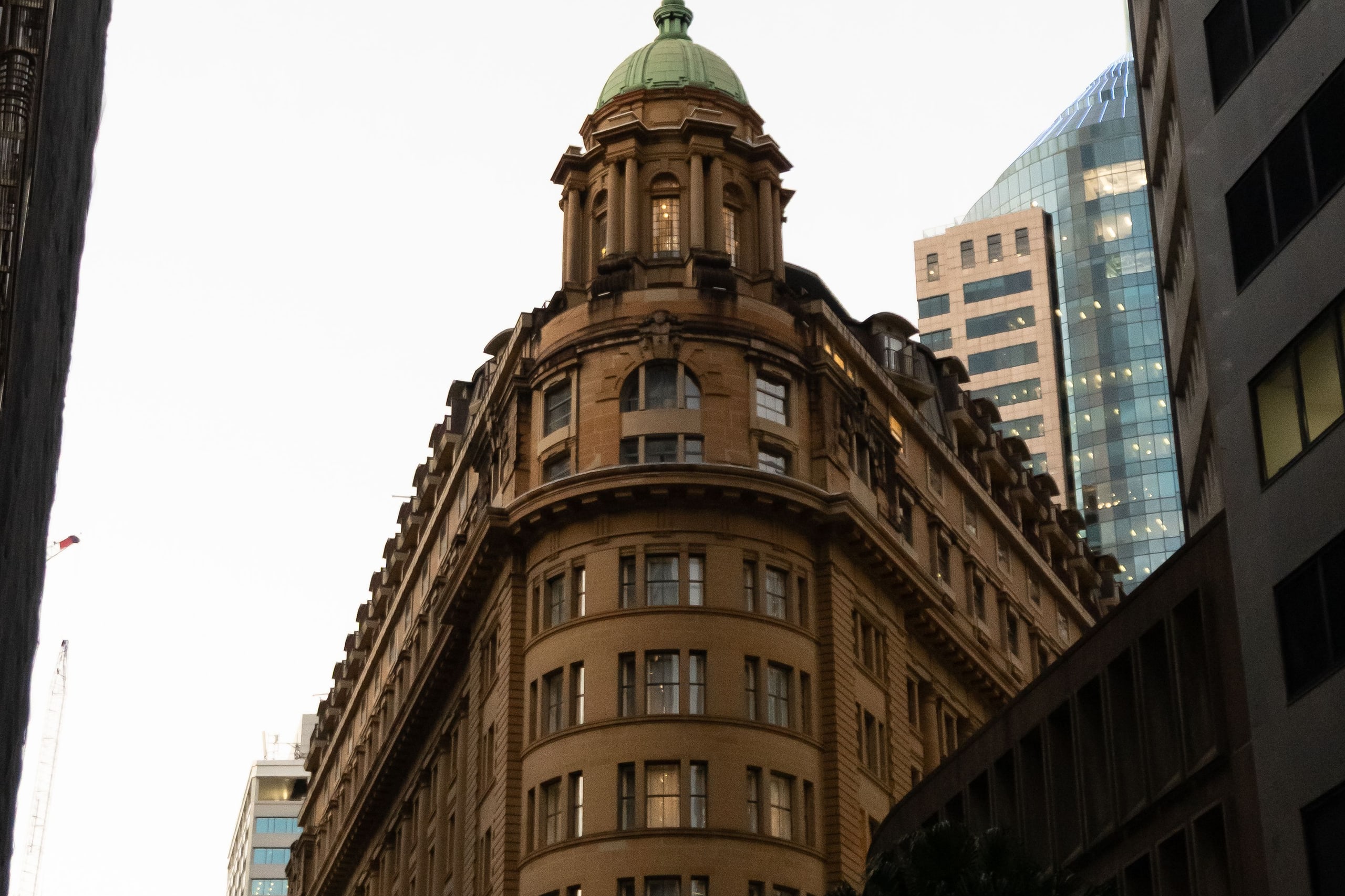 A heritage sandstone building with a copper dome in the Sydney central business district, glass towers rising behind
