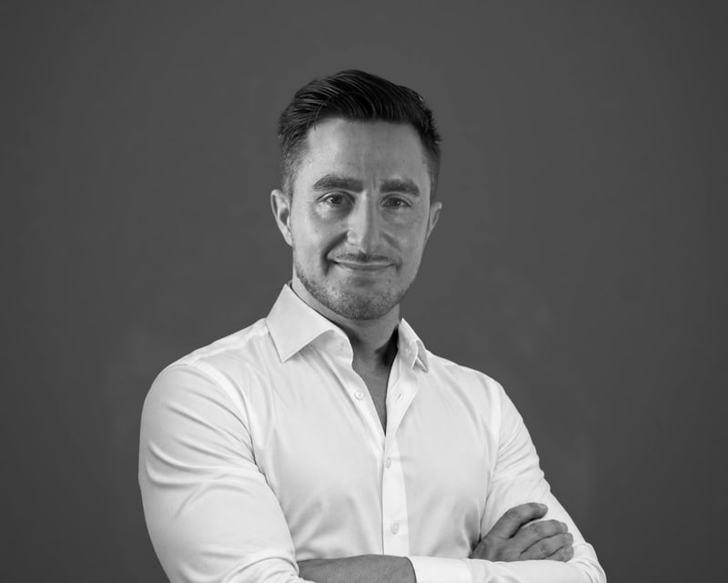 Black-and-white studio portrait of Michael Themis in a white shirt, arms folded
